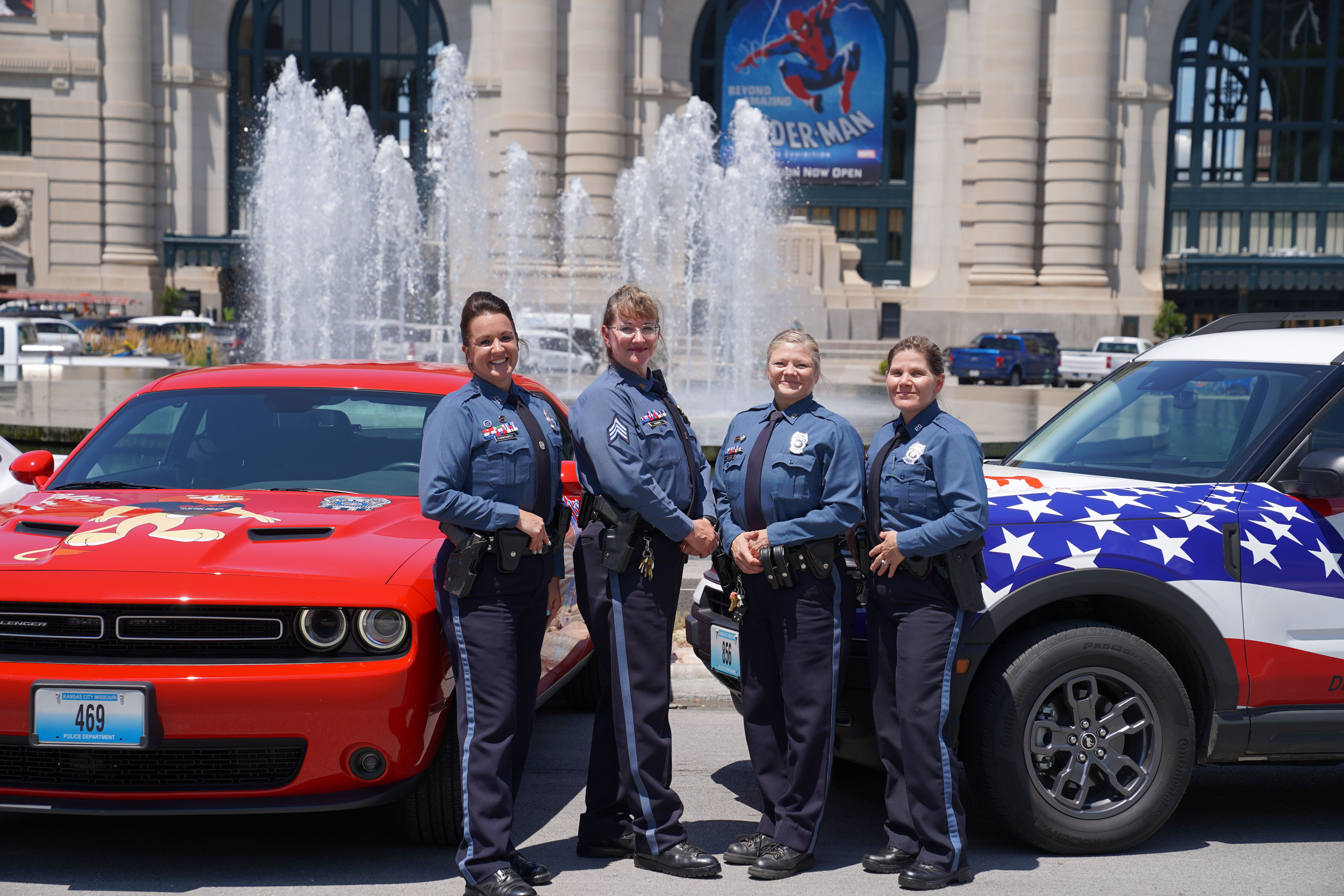 Four DARE and GREAT Officers in uniform, posing with their vehicles in front of Union Station.